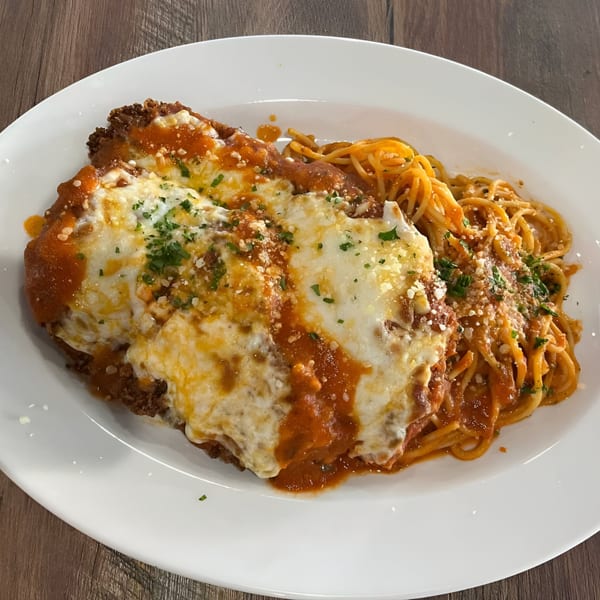 Chicken parmesan with melted cheese and marinara sauce, served alongside spaghetti on a white plate.