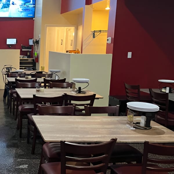 Interior of Milans Pizza dining area with empty tables and chairs, red walls, and a TV screen.