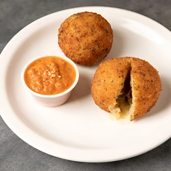 Two golden-brown arancini balls, one split open, with a side of marinara sauce on a white plate.