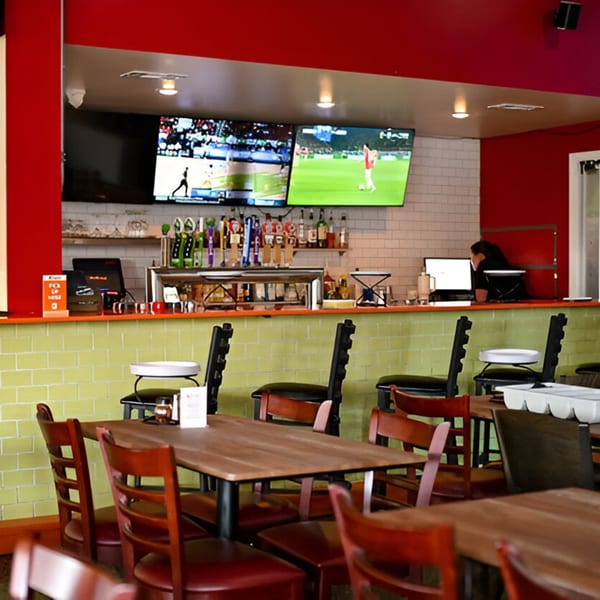 Interior of Milans Pizza with a bar, multiple TVs showing sports, and dining tables with chairs.