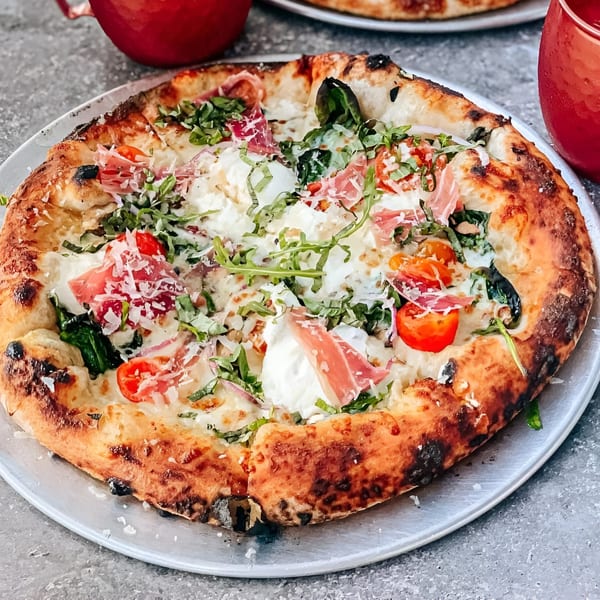 A Milans Pizza pie, topped with prosciutto, burrata, cherry tomatoes, arugula, and grated cheese.