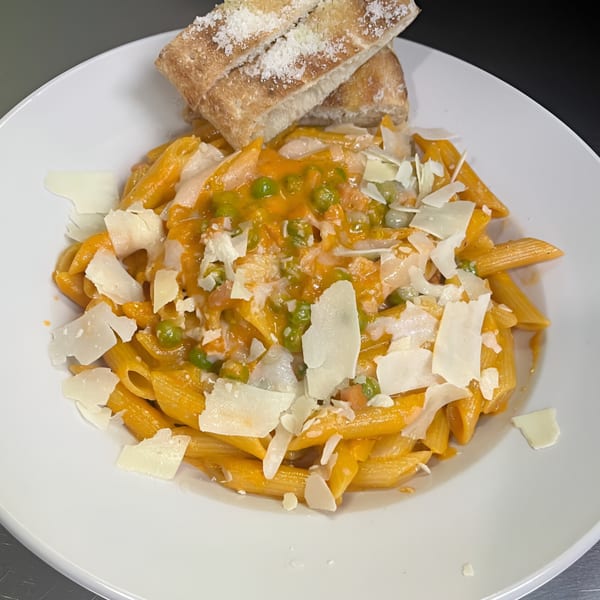 Penne pasta with orange sauce, green peas, and shaved Parmesan cheese, served with bread.