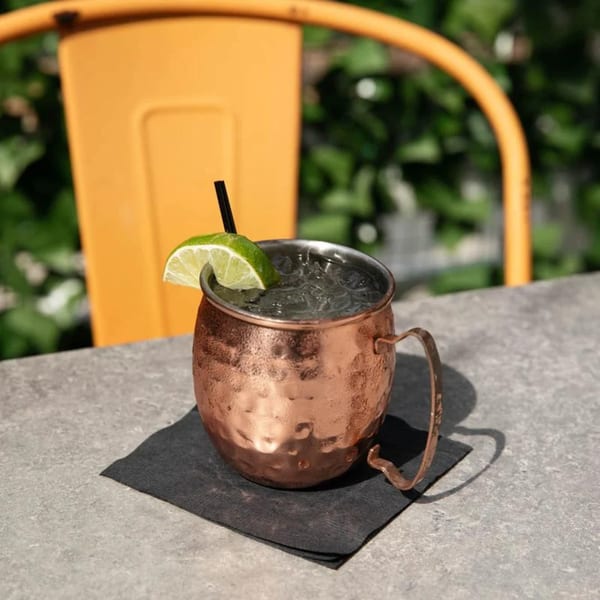 A copper mug filled with ice and a drink, garnished with a lime wedge and black straw.