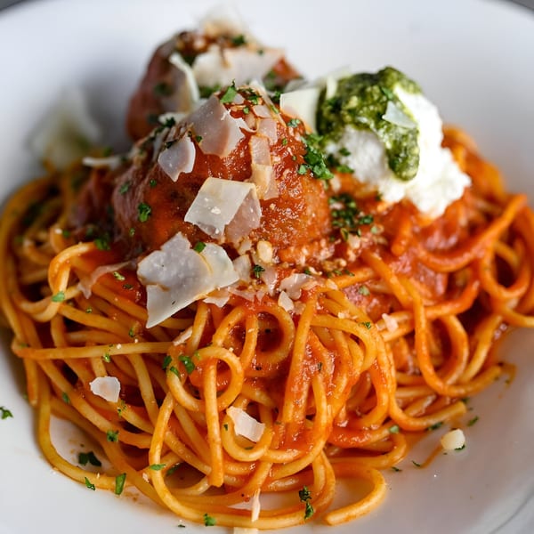 Spaghetti and meatballs with tomato sauce, parmesan, ricotta, and pesto on a white plate.