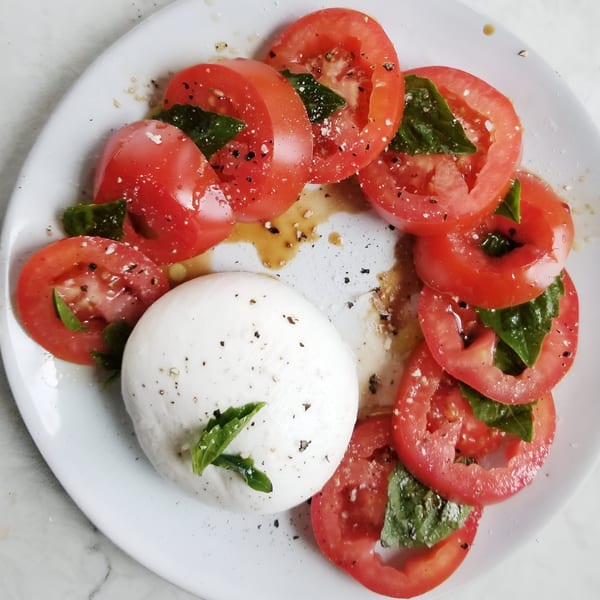 Caprese salad with sliced tomatoes, fresh mozzarella, basil leaves, and balsamic glaze on a white plate.