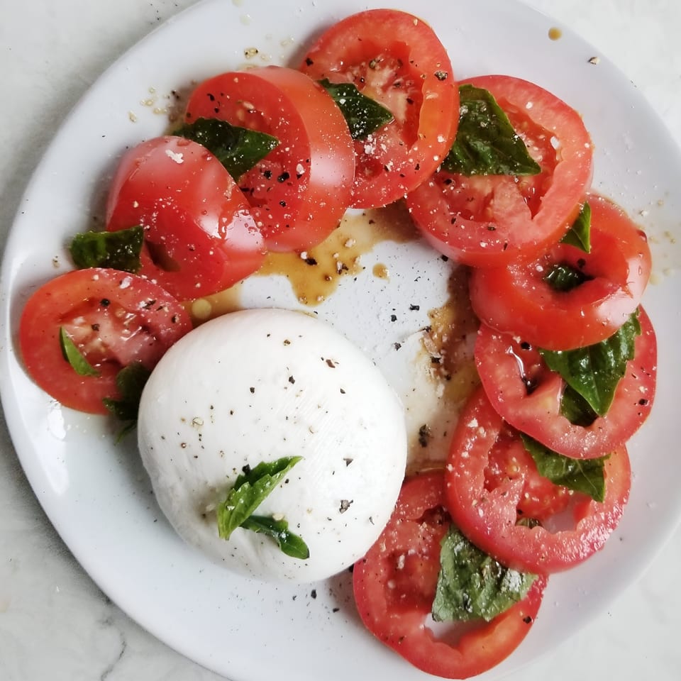 Caprese salad with sliced tomatoes, fresh mozzarella, basil leaves, and balsamic glaze on a white plate.