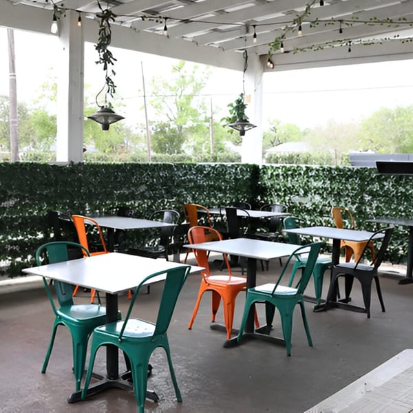 Outdoor patio with white tables and colorful chairs, surrounded by a green ivy wall.